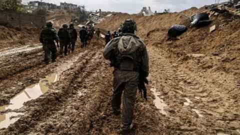 A group of armed soldiers wearing tactical clothes along a muddy, decorated war, surrounded by destroyed buildings and debris