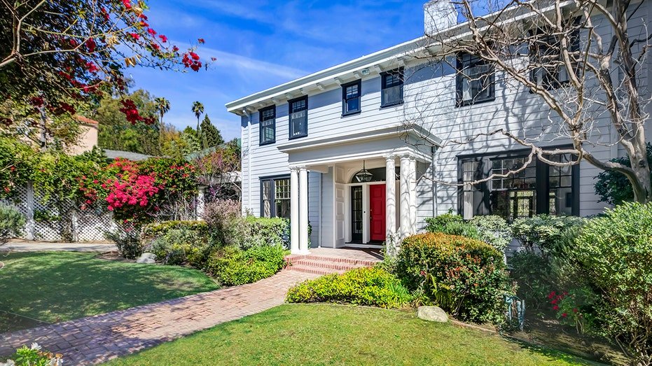 White home house with red door and lush grass on both sides of the brick corridor.