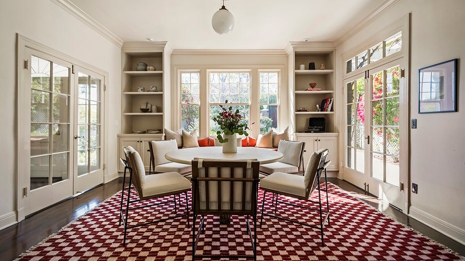 The dining room features a circular table and a large red and white rug.