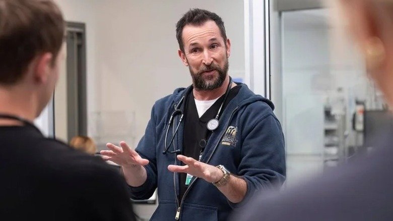 Noah Wail, as Dr. Ruby explains something for two people facing the camera in a house