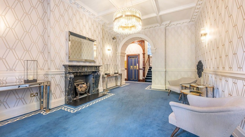 The entrance to the building includes a blue carpet, a fireplace and a seating area.