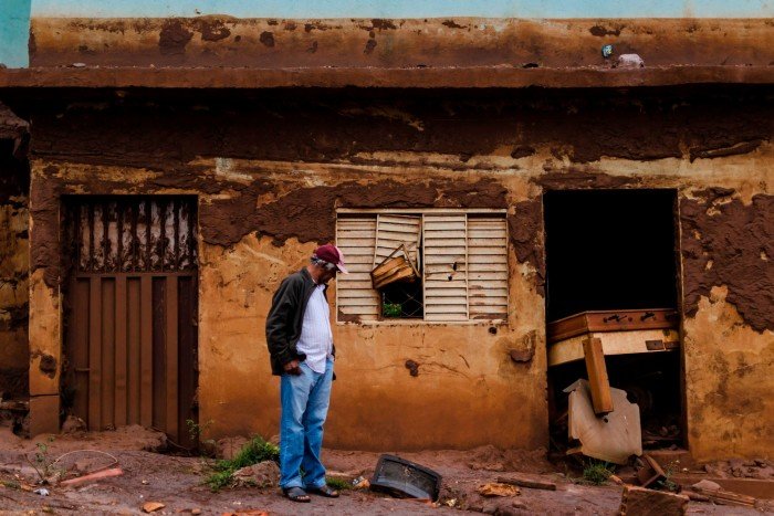 A man stands in front of his damaged house in the Bento Rodriguez, Mariana. The bottom of the building is covered with mud, with a widespread debris