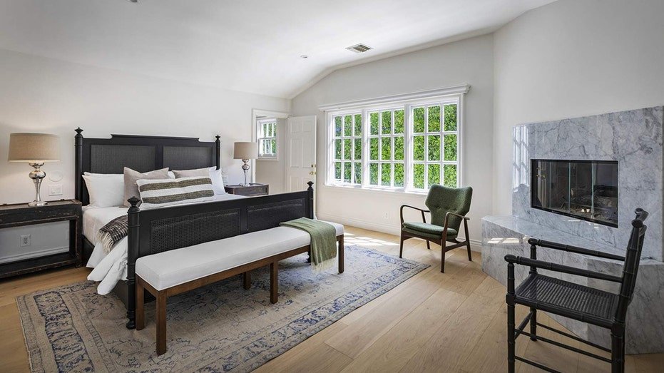 The basic bedroom features a large window and a burning fireplace.