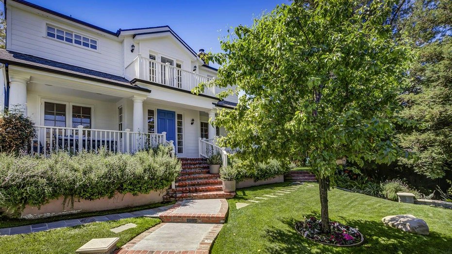 A stone corridor with leafy green grass on both sides leads to the front door of the house.