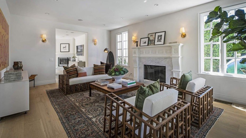The second living room also features a fireplace as well as wooden furniture with white cushions.