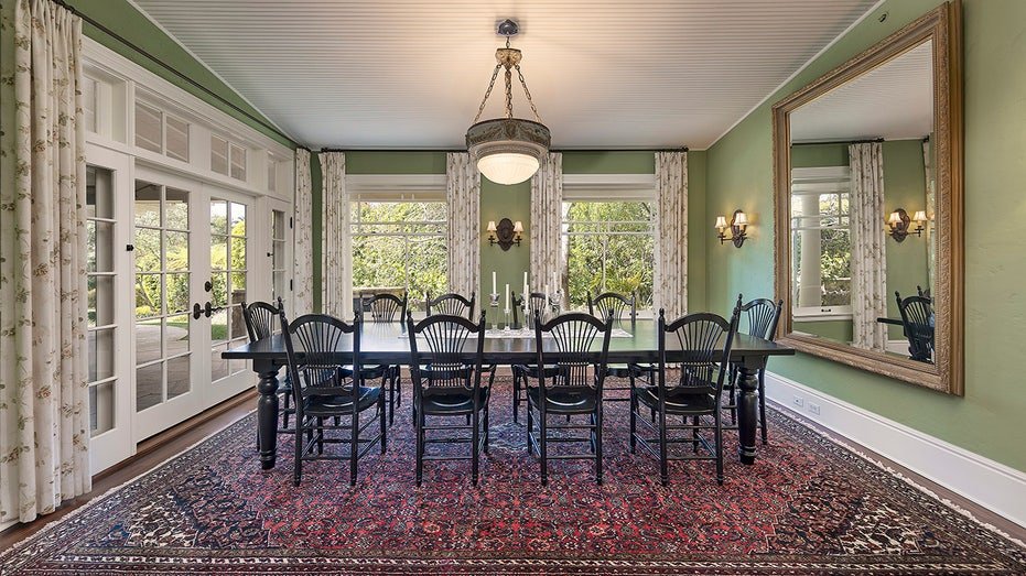 The dining room features green walls and windows extending from floor to ceiling and many windows.
