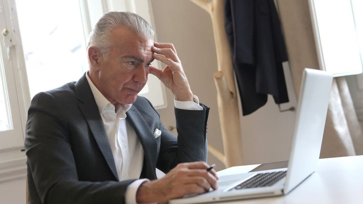 The tired businessman holds his head while he is on his computer