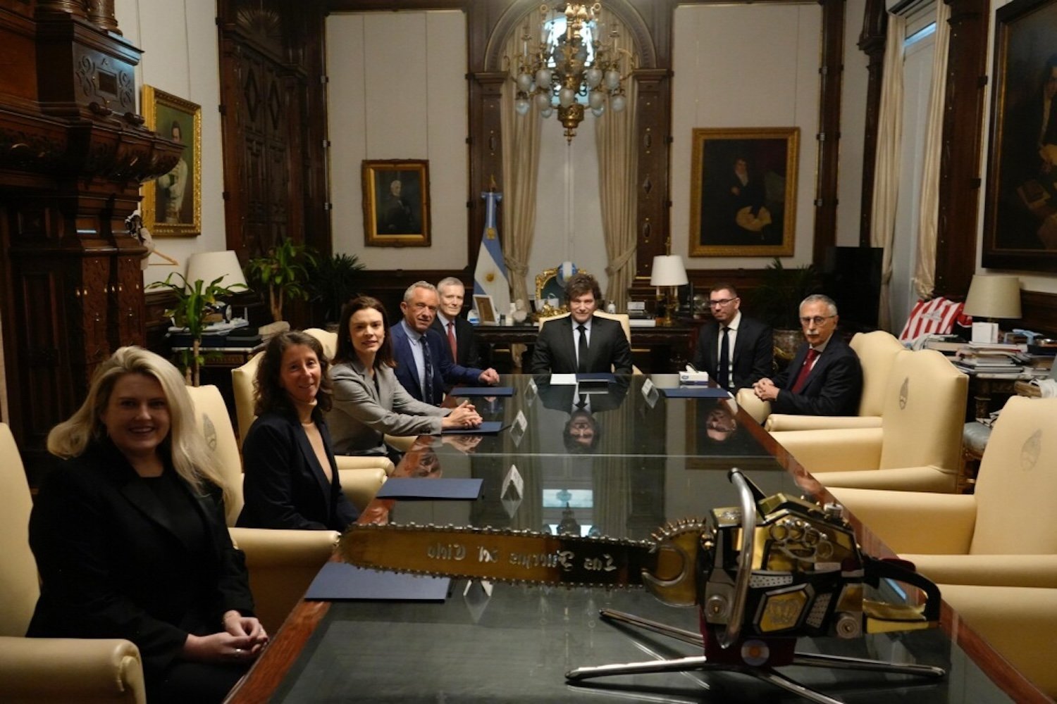 A group of people sitting around a table, including RFK JR. And Javier Milei, with a saw on the table in front of them.
