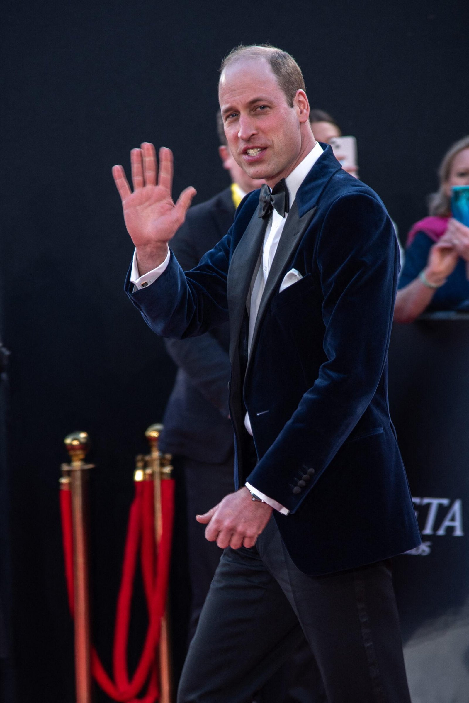Prince William wears a suit waving his right hand.