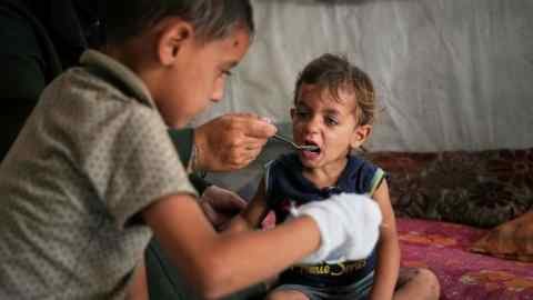A young boy is fed by his mother with food from a community kitchen in a Mawasi camp for the displaced Palestinians in Khan Yunis, south of Gaza