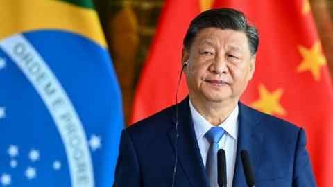 Xi Jinping stands on a platform with an ear headphone in front of the Brazilian and Chinese flags during a press conference