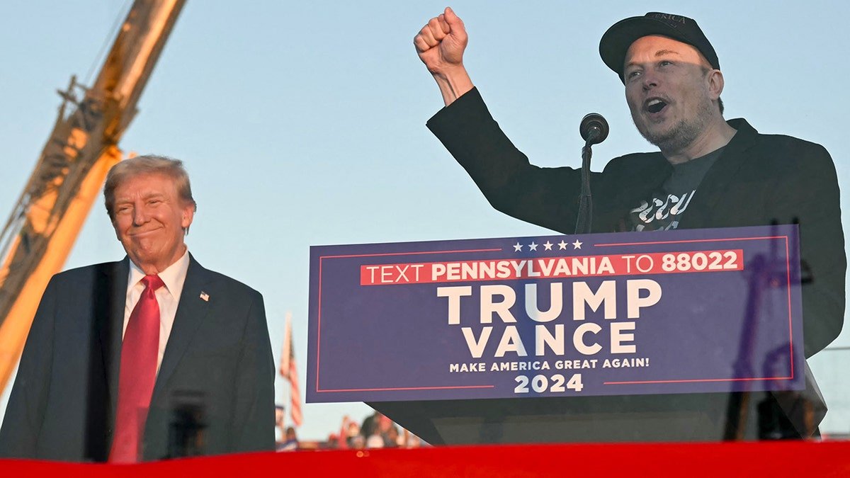 Elon Musk speaks while Donald Trump stands in the background