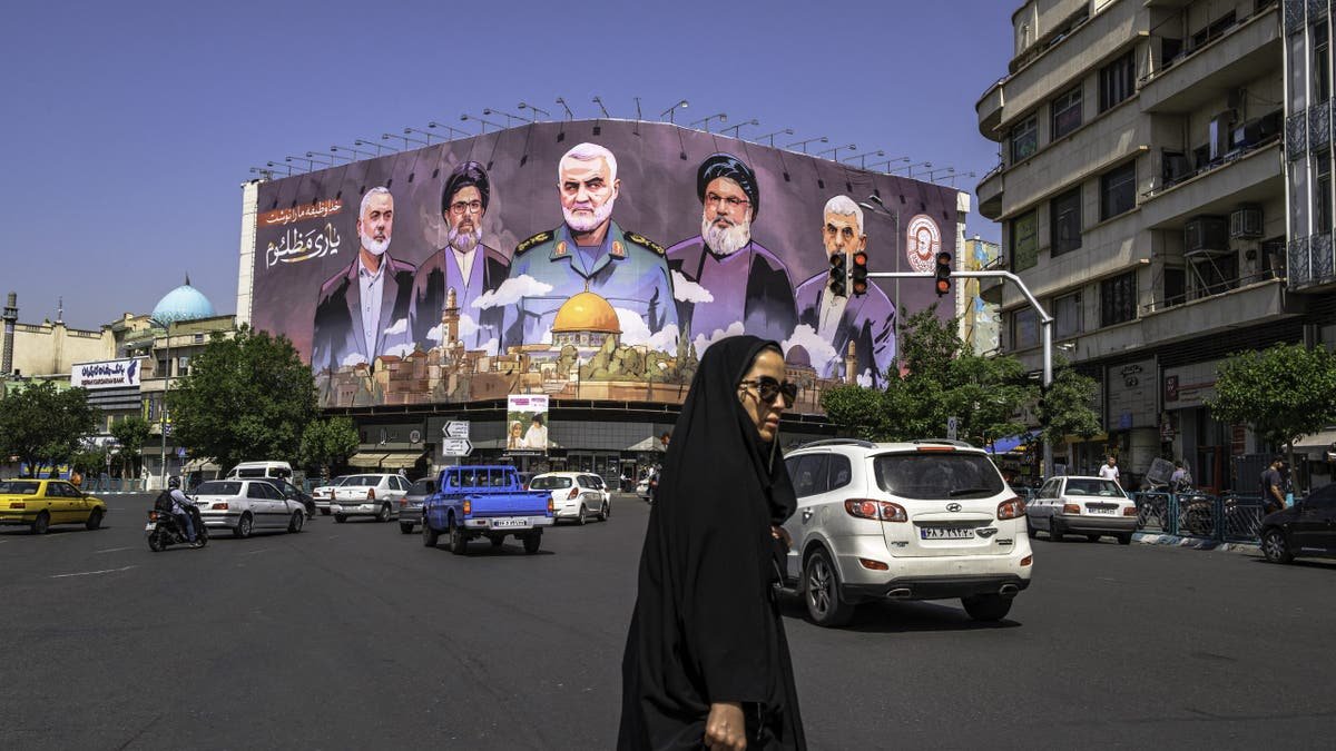 A giant mural in Iran in the background, a woman in black in the foreground