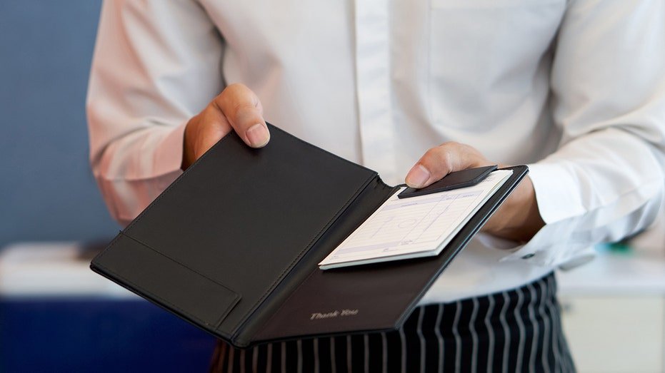 The waiter in a white shirt and an apron is given a receipt after calling the bill.