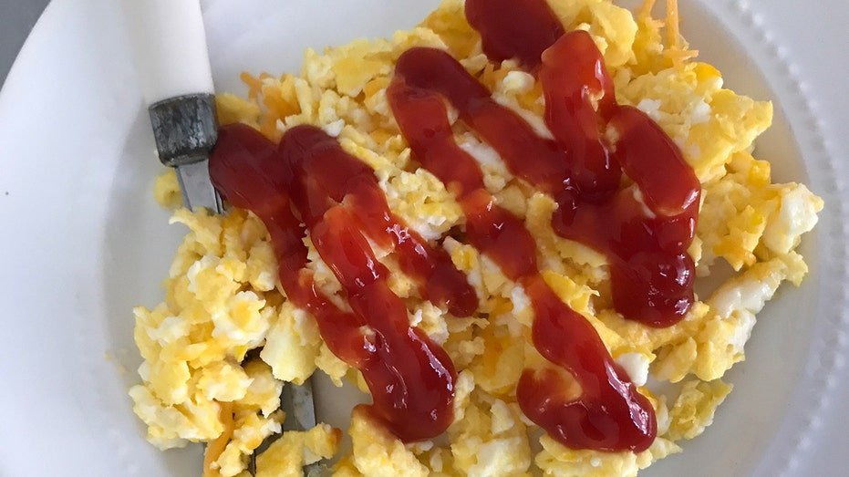The ketchup spreads on the scrambled eggs on a white plate.