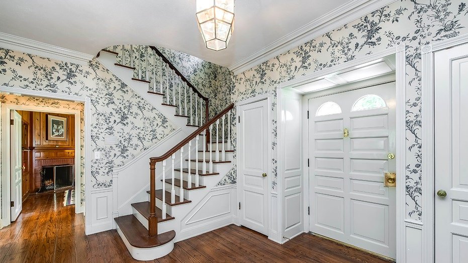 The entrance is characterized by paper with marine blue designs, as well as floors of solid wood and a staircase that leads to the upper floor.