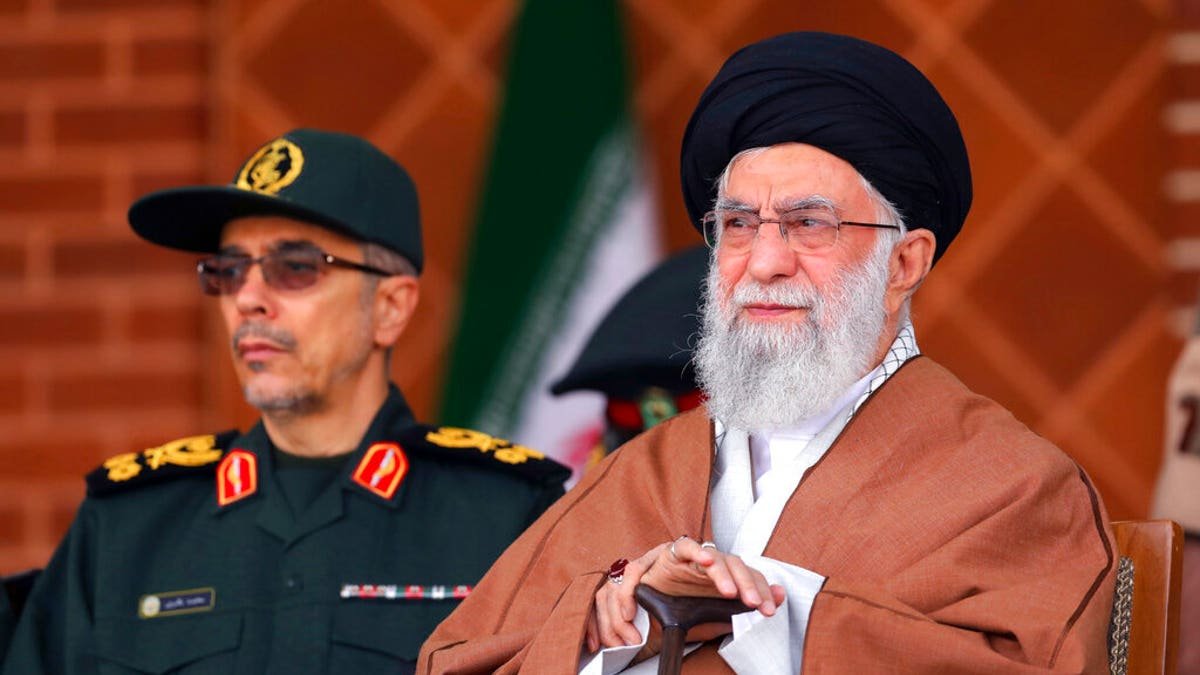 Supreme Leader, Ayatollah Ali Khamenei, sits on a chair and looks at him while an Iranian soldier stands behind him