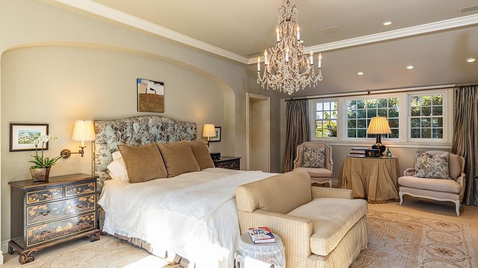 The basic bedroom has a chandelier in the center of the room as well as windows.