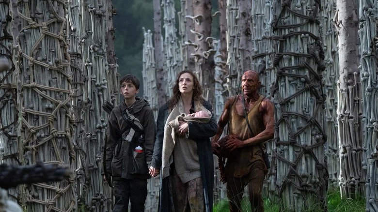Spike, ISLA (carrying a child), and Dr. Ian Kilson stands between many bones after 28 years