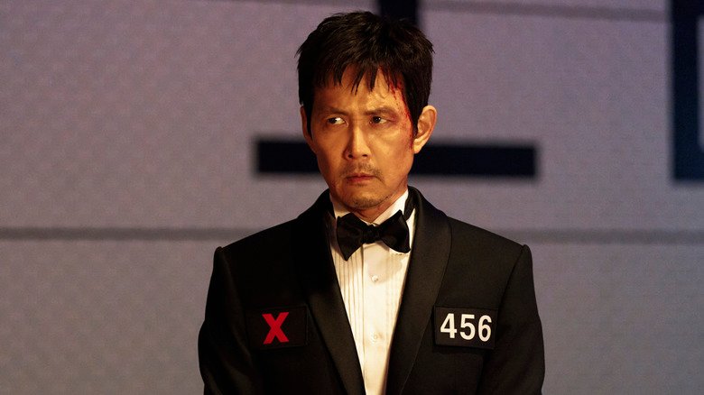 Gi-Hun wears an evening and sits at a dinner table at Squid Game Season 3
