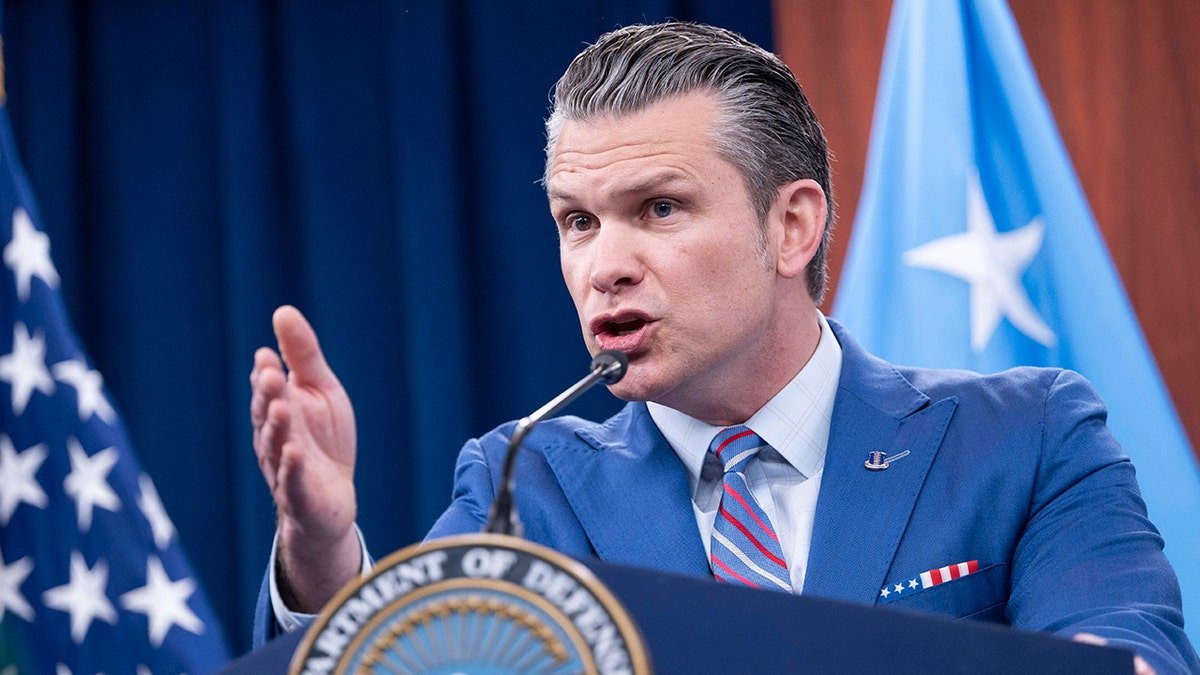 Defense Minister Beit Higseth wears a blue suit and indicates his hand