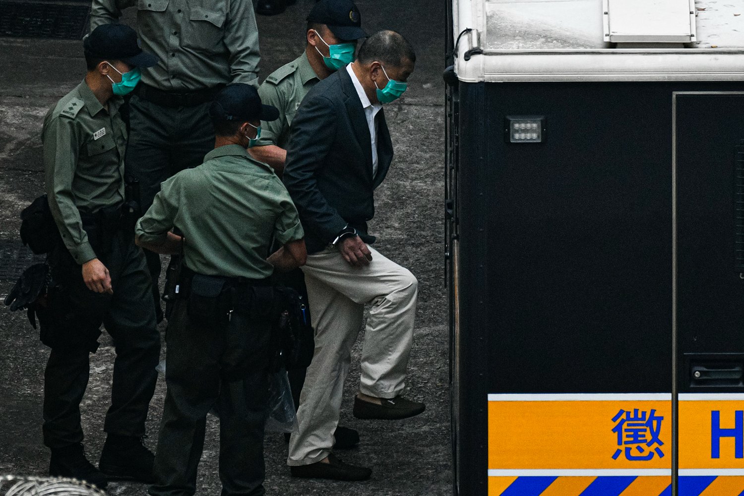 Four security guards are surrounded by uniform, conforming standardized shirts and facial masks, Jimmy Lay, as it rises to enter the back of the car. For any man in the seventies of his life wearing pants khaki, dark suit jacket, face mask, and handcuffs.
