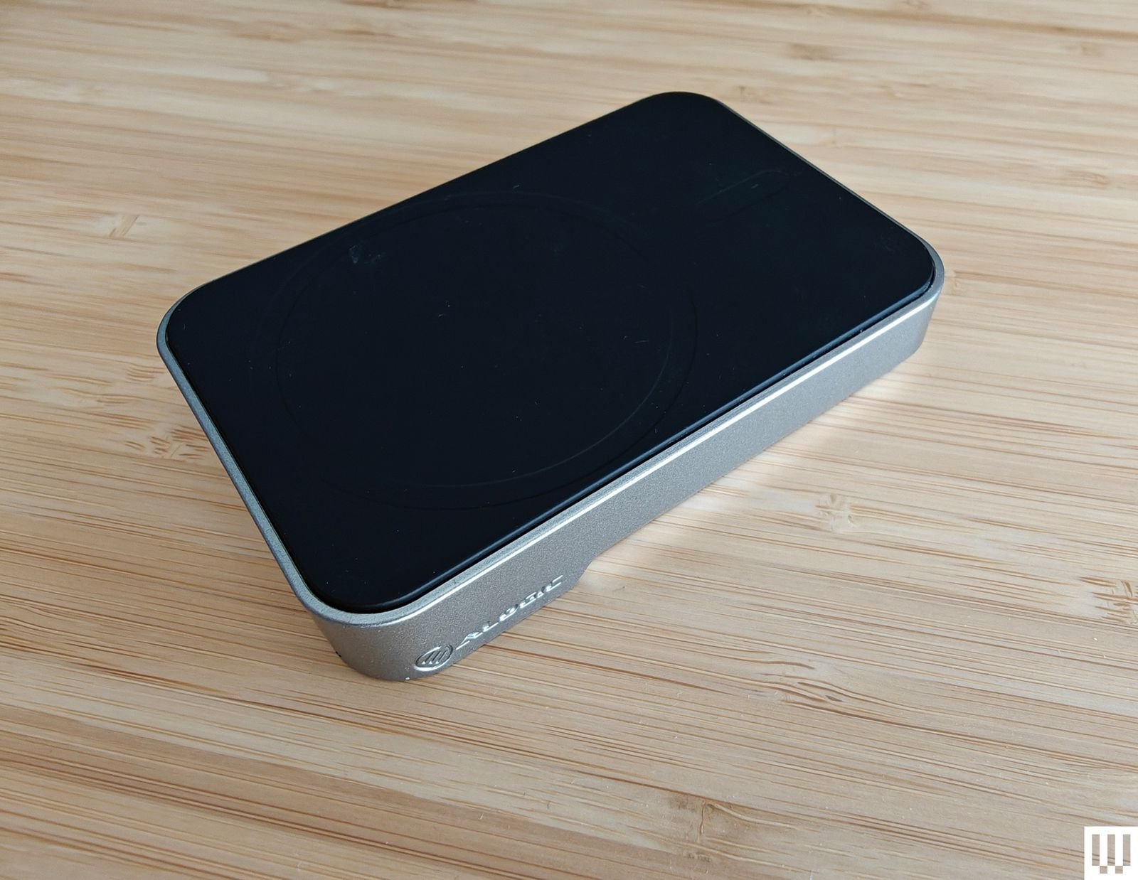 Magsafe rectangular power bank with black round edges on top and silver on both sides sitting on a wooden surface