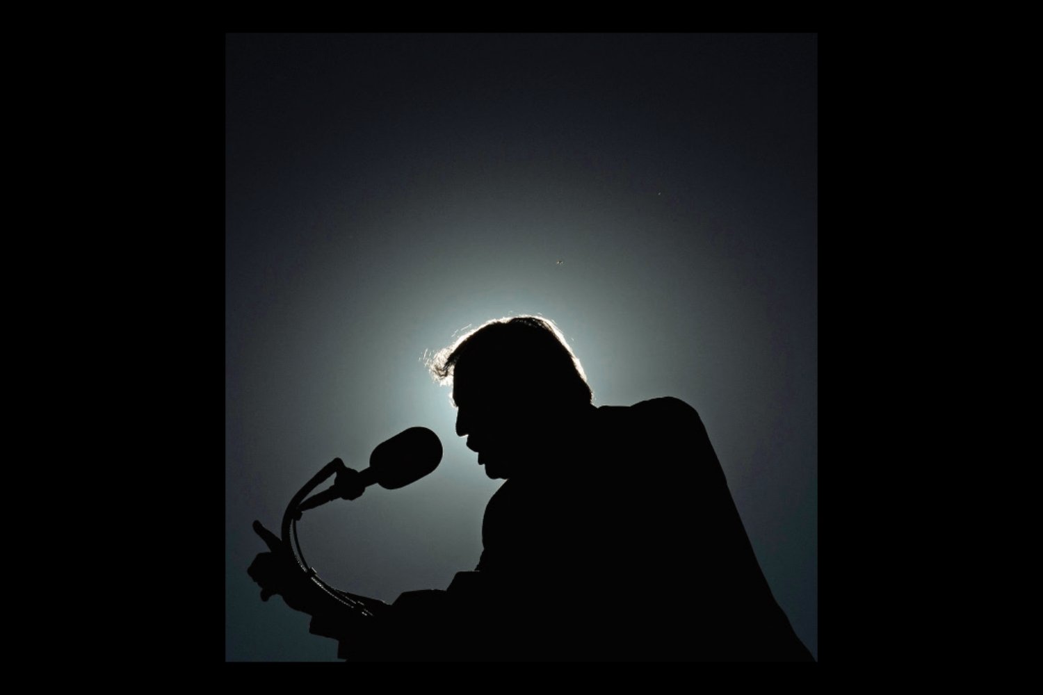An image of Donald Trump silhouetted against a halo of light as he speaks into a microphone. The photo is inset on a black background.