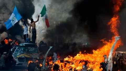 The demonstrators wave the flags while burning cars lined up on the street