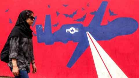 A woman walks next to a mural drawn on the exterior walls of the former American embassy in Tehran