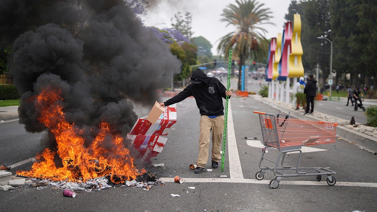 A man throwing cardboard on fire on the street