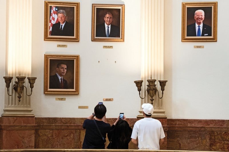 People use their phones to take a picture of the empty space on a wall of pictures.