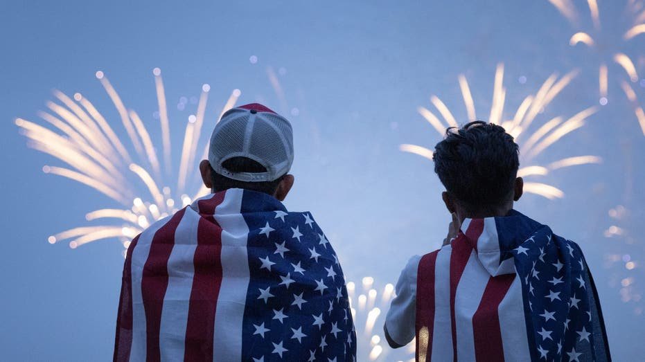 Two people wear American flags while watching fireworks