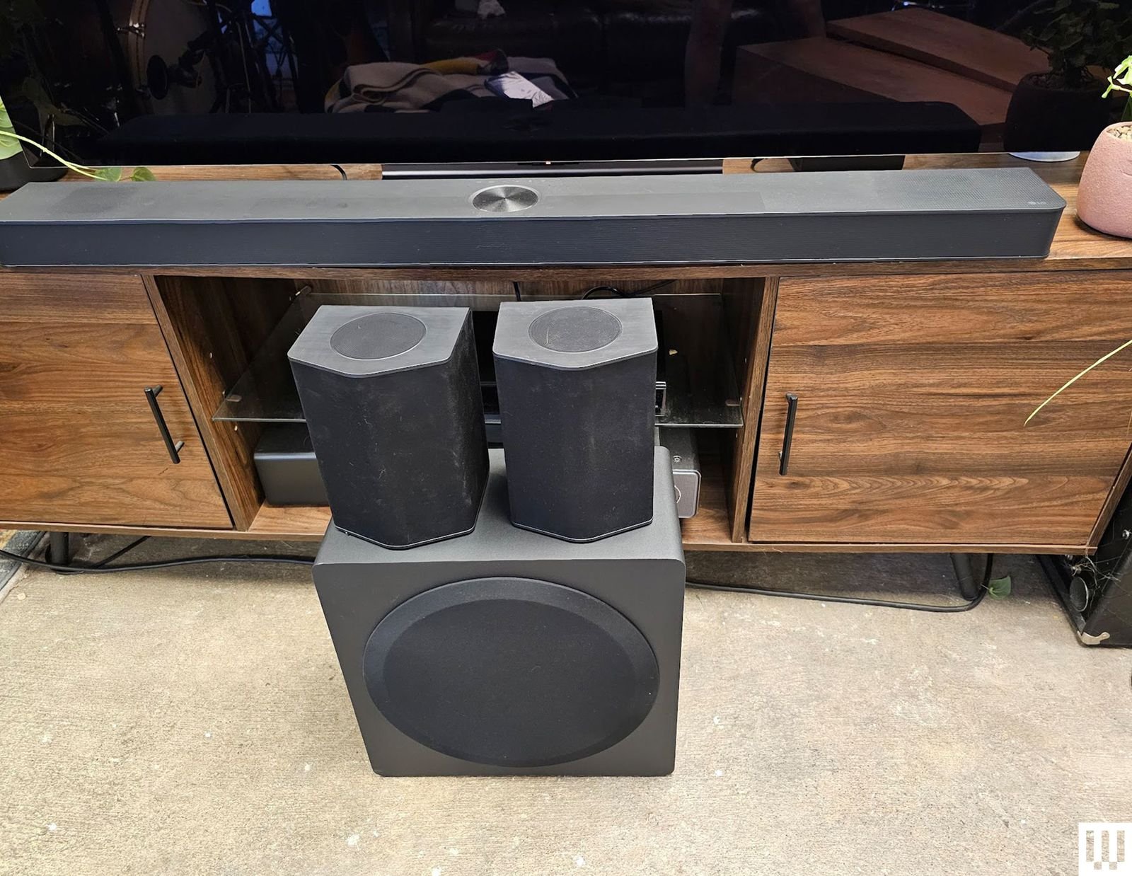 Long flat speaker on Credenza behind a square speaker on the floor with two smaller loudspeakers on top