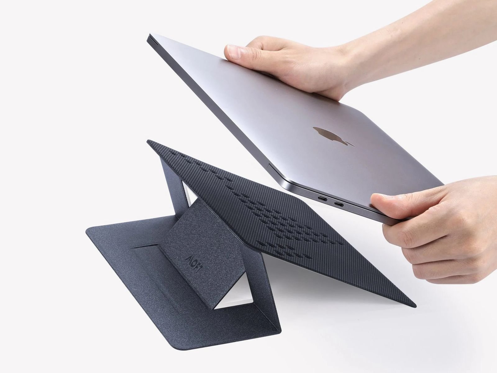 MOFT Invisible Stand, which is a black laptop from angular with its hands with a silver laptop, is about to put it on top