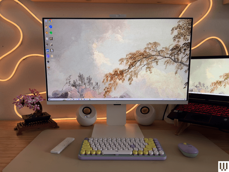 White flat screen monitor on desk with 2 speakers on either side, neon lighting behind, and picture of sky and leaves looking upward on the screen