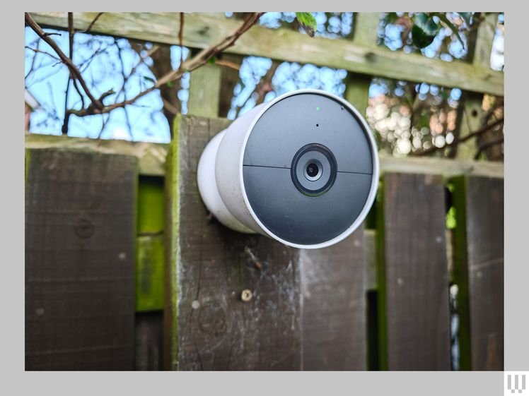 White and grey cone-shaped security camera attached to a wooden fence