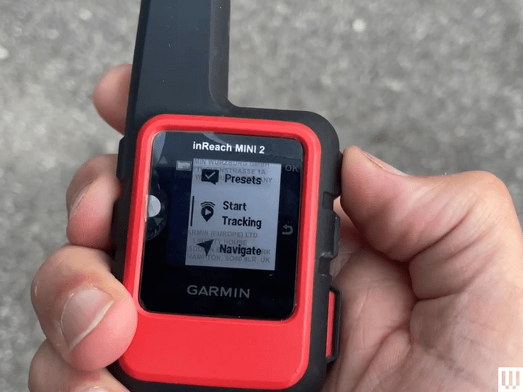 Hand holding small black and red device with a thick antenna and small screen