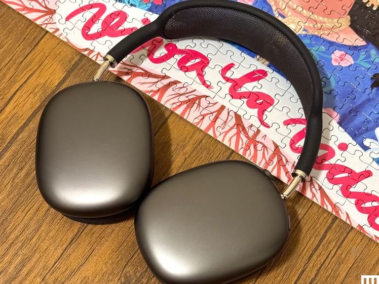 Light grey AirPods Max headphones with black strap placed partially on a puzzle