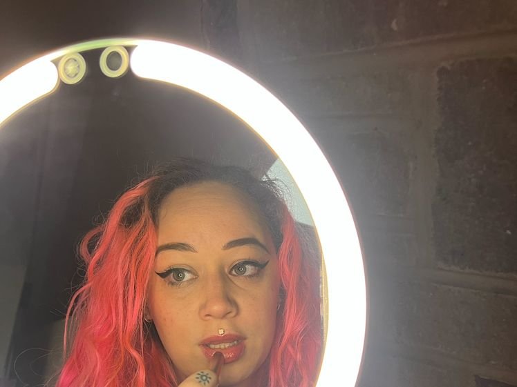 Fancii Abigail, a circular light-up makeup mirror on a stand with the top reflection showing someone with pink hair putting on lipstick