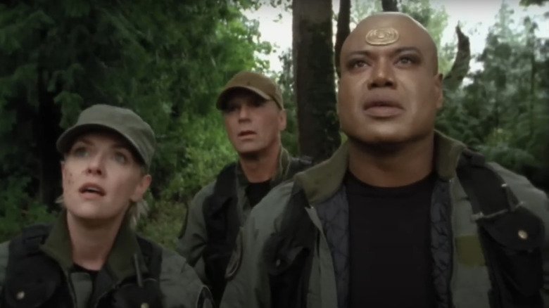 Samantha Carter from Amanda Taber stands alongside Jacques O'Neill from Richard Dean Anderson and Christopher Godz in a forest in Stargit SG-1