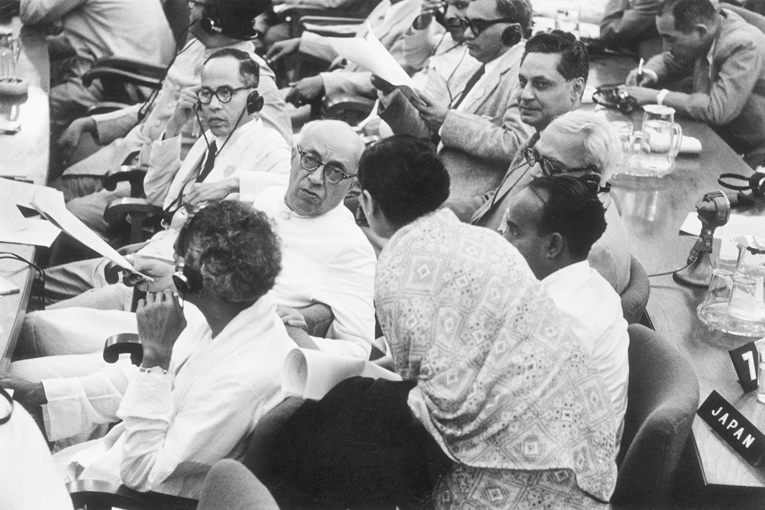 Nehru's return to consultation with another delegate sitting in a crowd of people sitting in ranks.