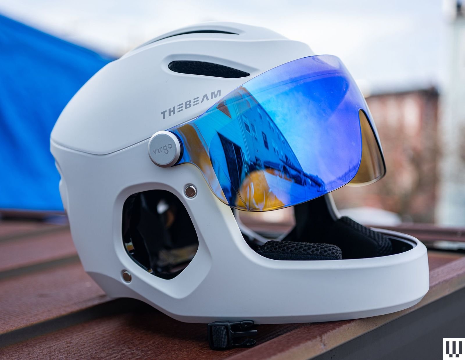 The Beam Virgo a white helmet with blue reflective lenses sitting on a wooden surface