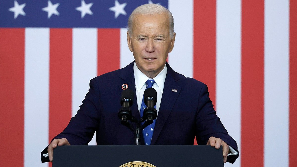 President Joe Biden stands in front of the background of the American flag