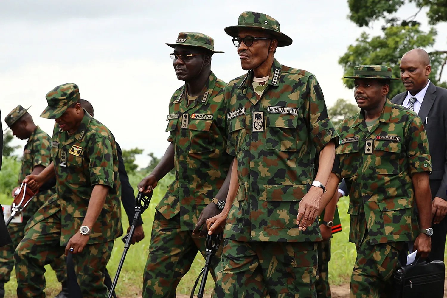 Muhammadu Buhari, dressed in camouflage fatigues and a camouflaged hat, walks with others also in fatigues.