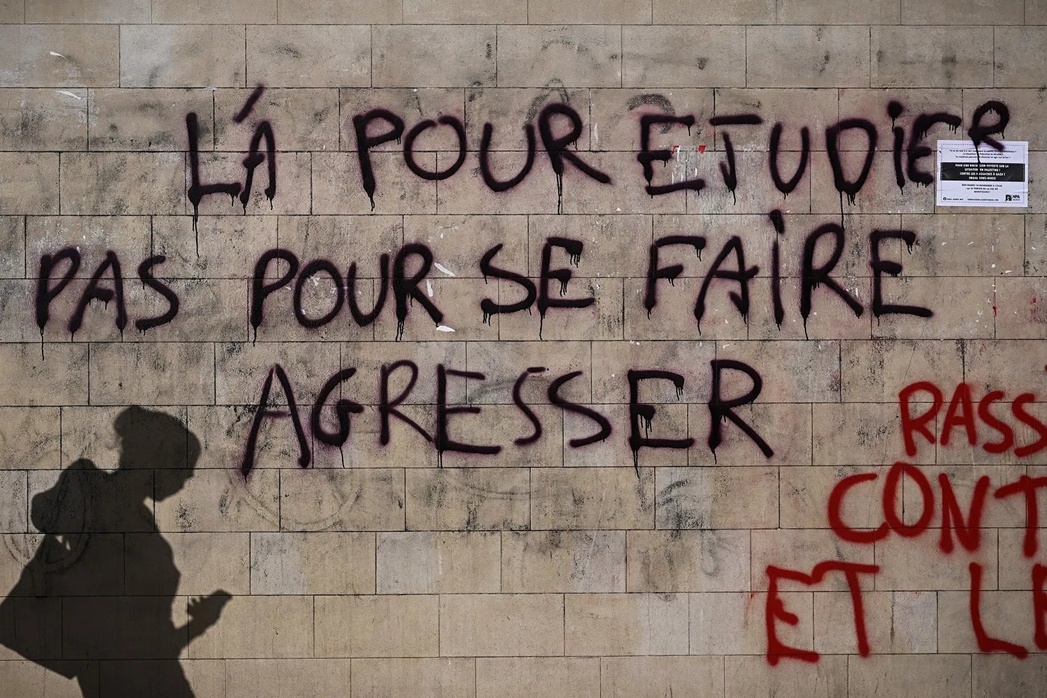 Graffiti words in French on a wall with a student silhouetted as they walk past.