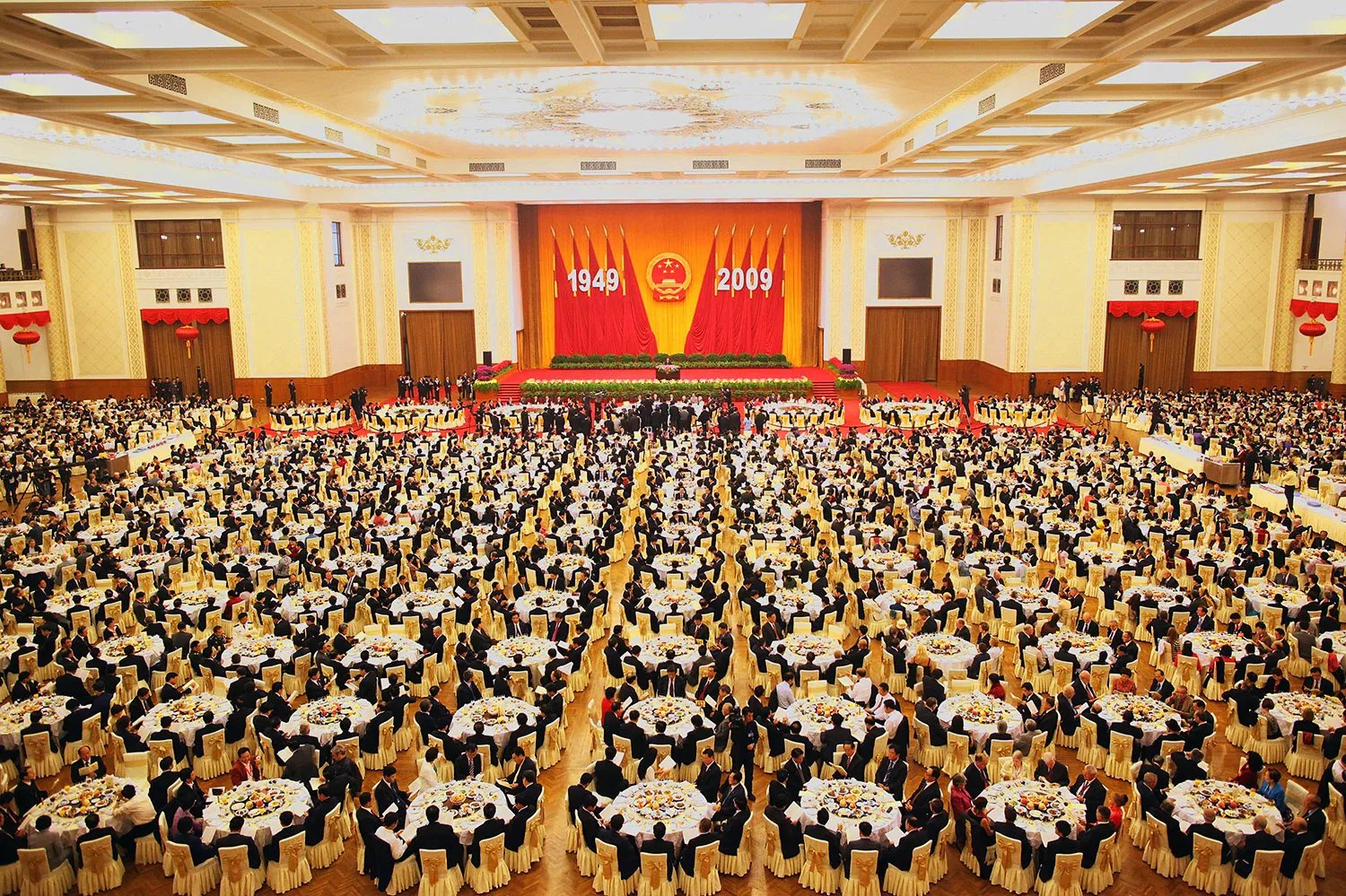 A large official hall full of people around hundreds of circular tables.