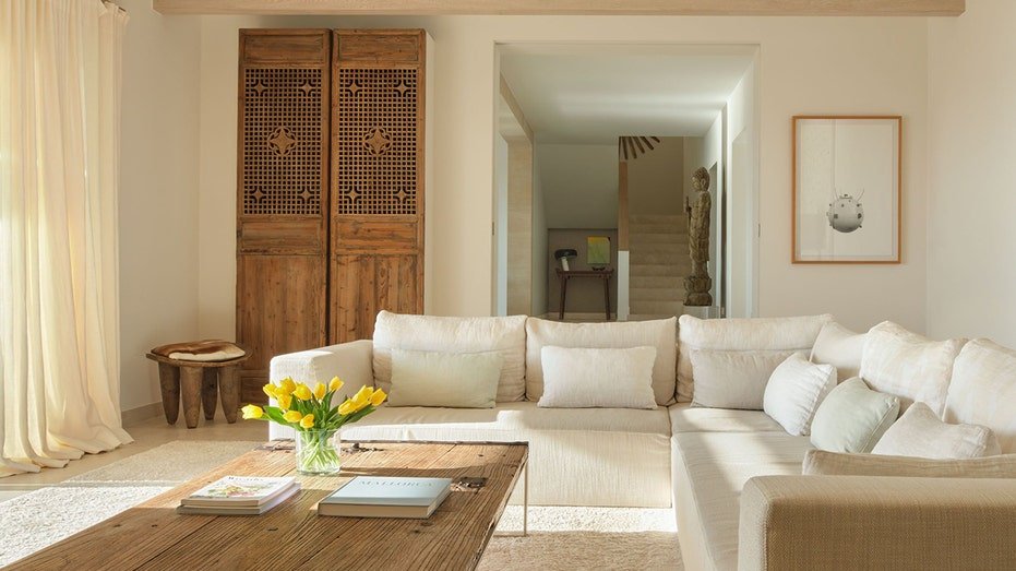 A living room with a white sectoral sofa and a wooden wardrobe.