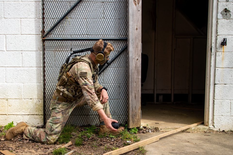 A uniformed soldier, kneeling, gets ready to toss a camera