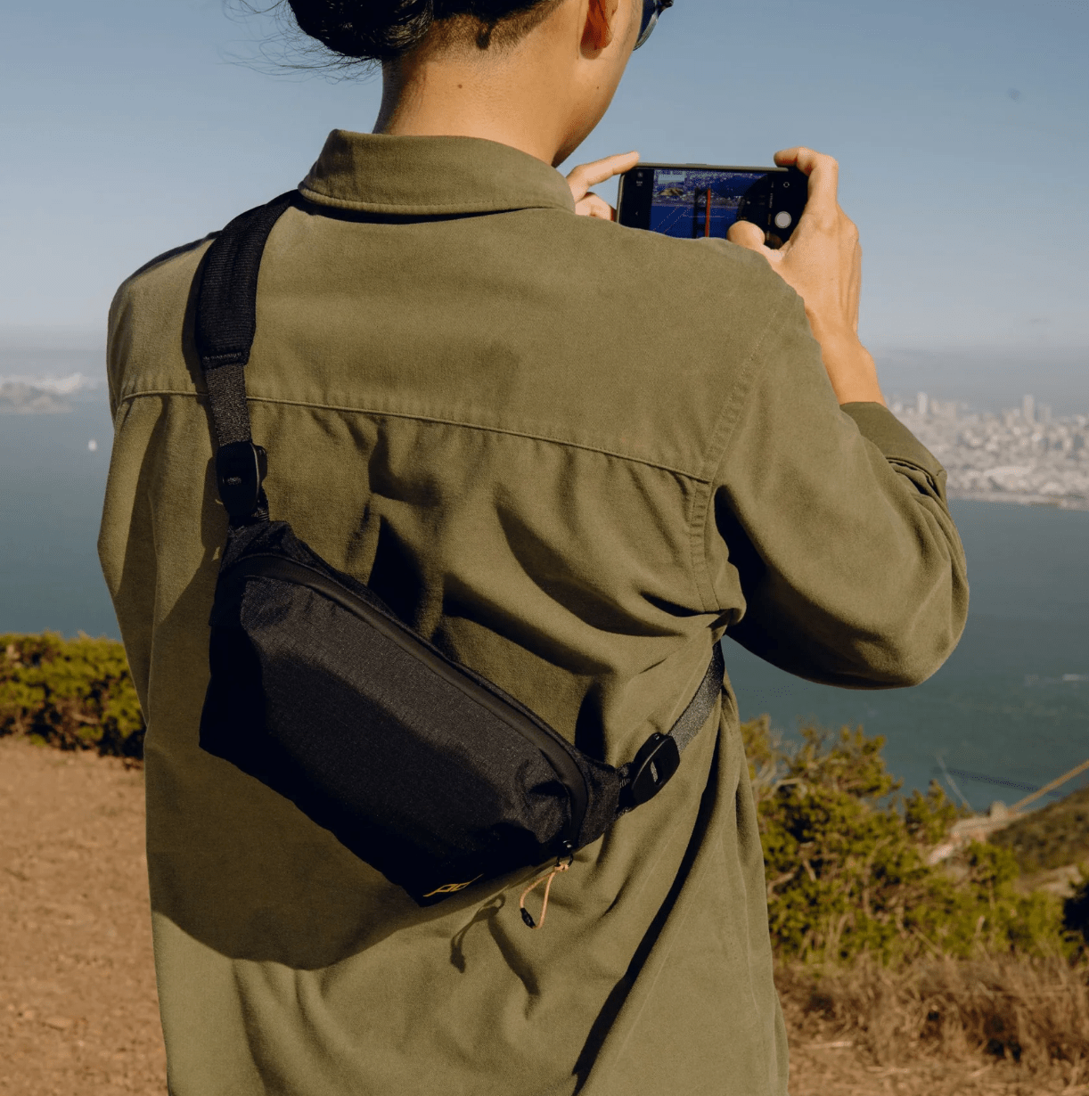 Person with camera looking out at landscape with sling across their back.